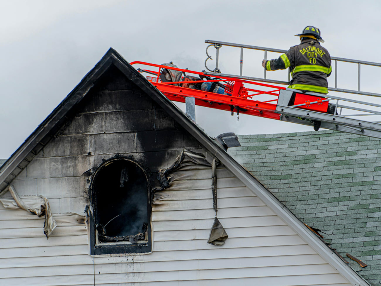 Fireman on a ladder above a burned house attic window